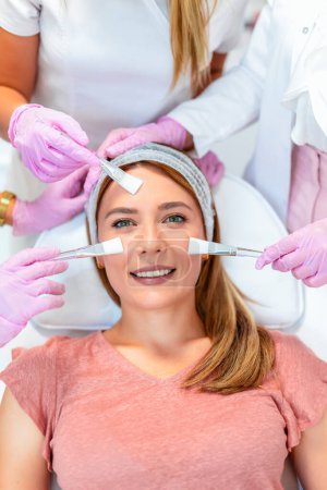 Foto de Tres médicos y cosméticos haciendo múltiples tratamientos faciales en la cara de una mujer joven - Imagen libre de derechos