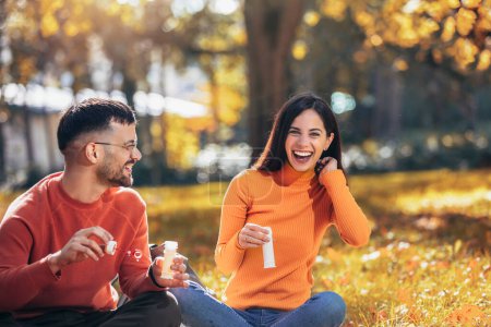 Téléchargez les photos : Couple soufflant des bulles et s'amusant. Journée ensoleillée d'automne dans le parc coloré - en image libre de droit