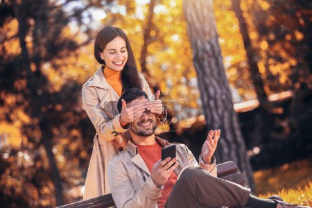 Téléchargez les photos : Petite amie surprenant son petit ami dans un parc un jour d'automne ensoleillé - en image libre de droit