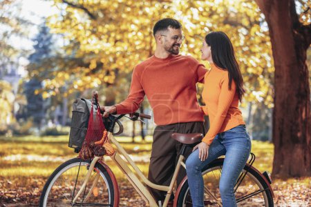 Foto de Feliz pareja joven montando en bicicleta en un día soleado de otoño. El parque es colorido - Imagen libre de derechos