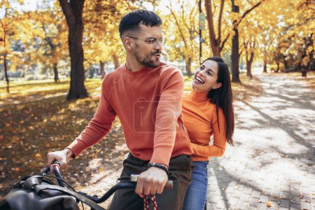 Téléchargez les photos : Heureux jeune couple en vélo par une journée ensoleillée d'automne. Le parc est coloré - en image libre de droit