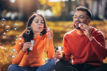 Téléchargez les photos : Couple soufflant des bulles et s'amusant. Journée ensoleillée d'automne dans le parc coloré - en image libre de droit