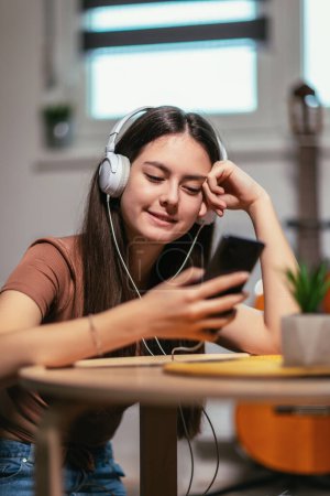 Foto de Beautiful teenager girl surfing social media on smart phone while having leisure time at her home. - Imagen libre de derechos
