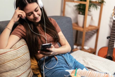 Téléchargez les photos : Beautiful teenager girl surfing social media on smart phone while having leisure time at her home. - en image libre de droit