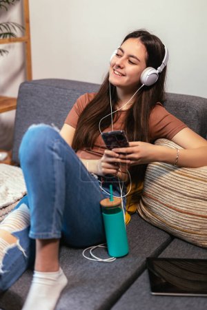 Foto de Beautiful teenager girl surfing social media on smart phone while having leisure time at her home. - Imagen libre de derechos