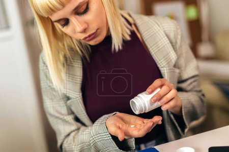 Foto de Mujer sentada junto al escritorio en la oficina y tomando pastillas médicas - Imagen libre de derechos
