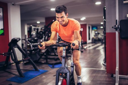 Photo for Man biking in the gym, exercising legs doing cardio workout cycling bikes. - Royalty Free Image