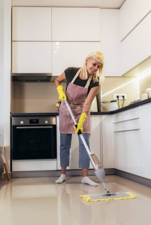 Photo for Young blonde woman cleaning a kitchen floor - Royalty Free Image