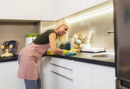 Téléchargez les photos : Jeune femme blonde nettoyer une cuisine - en image libre de droit