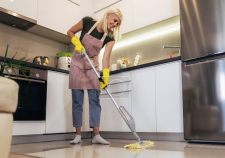 Foto de Mujer rubia joven limpiando un piso de cocina - Imagen libre de derechos