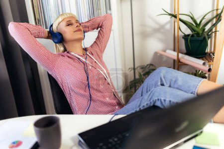 Téléchargez les photos : Jeune femme blonde frissonnant avec ses jambes sur la table pendant qu'elle écoute de la musique - en image libre de droit