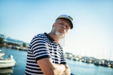 Téléchargez les photos : Homme mûr debout près de la mer vêtu d'une chemise et d'un chapeau de marin. - en image libre de droit