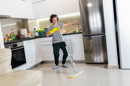 Photo for Male kid cleaning the floor and listening to the music. He is doing his chore and he is dancing - Royalty Free Image