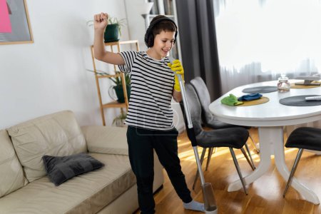 Photo for Male kid cleaning the floor and listening to the music. He is doing his chore and he is dancing - Royalty Free Image