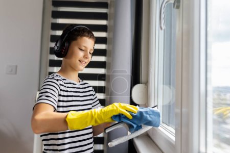 Téléchargez les photos : Homme enfant nettoyer la fenêtre avec le spray et porter le casque tout en écoutant la musique - en image libre de droit