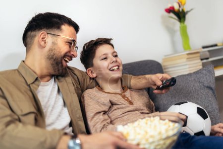 Téléchargez les photos : Père et fils regardant un match de football tout en mangeant du pop-corn. - en image libre de droit