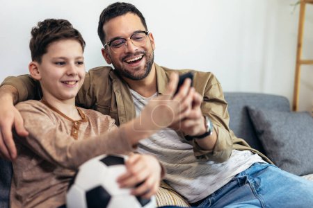 Téléchargez les photos : Père et fils regardant un match de football tout en mangeant du pop-corn. - en image libre de droit