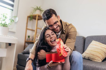 Foto de Man giving a surprise gift to woman at home. Party at home, birthday gift, anniversary, Valentines day and holiday - Imagen libre de derechos