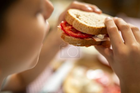 Foto de El chico está comiendo sándwich casero en casa. - Imagen libre de derechos