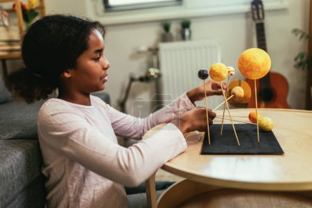 Téléchargez les photos : Happy african american school girl making a solar system for a school science project at home - en image libre de droit