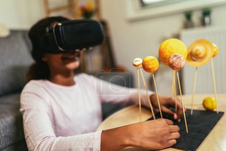 Téléchargez les photos : Happy african american school girl making a solar system for a school science project at home using VR glasses to immerse herself in metaverse - en image libre de droit