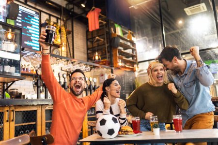 Foto de Emocionados aficionados al fútbol celebrando mientras ven el partido de fútbol en la televisión en el bar. - Imagen libre de derechos