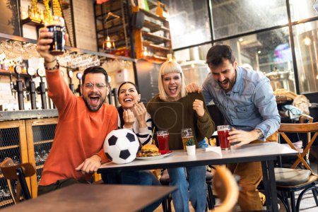 Foto de Emocionados aficionados al fútbol celebrando mientras ven el partido de fútbol en la televisión en el bar. - Imagen libre de derechos