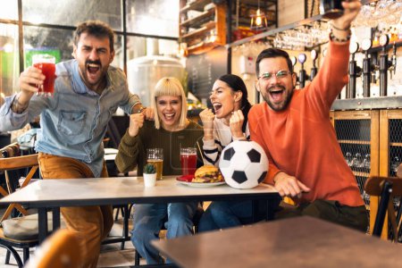 Téléchargez les photos : Fans de football excités célébrant tout en regardant le match de football à la télévision dans le bar. - en image libre de droit