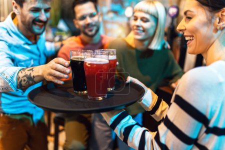 Téléchargez les photos : Jeune serveuse ou barman servant des boissons dans un bar portant un plateau avec de la bière - en image libre de droit