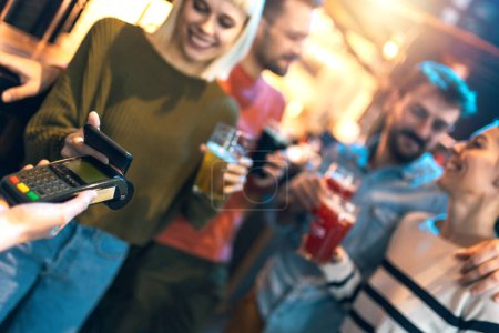 Téléchargez les photos : Diverse friends in bar paying with cellular device - en image libre de droit