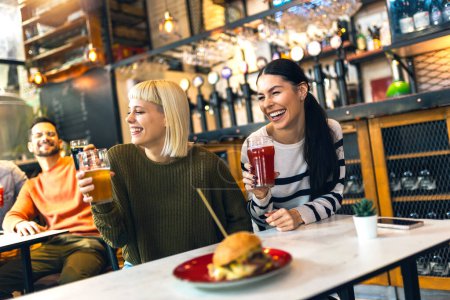 Foto de Sonrientes jóvenes amigos bebiendo cerveza artesanal en el pub - Imagen libre de derechos