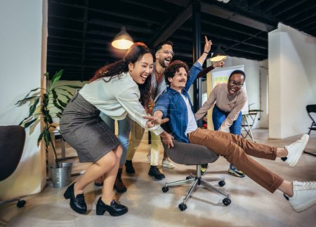 Young cheerful businesspeople in smart casual wear having fun while racing on office chairs and smiling