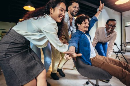 Foto de Jóvenes empresarios alegres en ropa casual inteligente divirtiéndose mientras compiten en sillas de oficina y sonriendo - Imagen libre de derechos