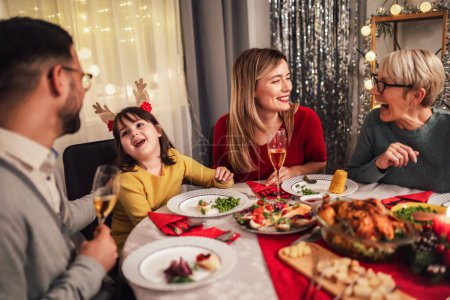 Foto de La foto captura el calor y la alegría de una cena de Navidad con una querida abuela, madre, padre e hija. La familia se reúne alrededor de la mesa festiva, sonriendo y riendo mientras disfrutan de una fiesta tradicional de pavo, relleno, y todo el - Imagen libre de derechos