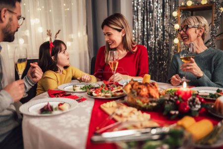 Téléchargez les photos : Photo capture la chaleur et la joie d'un dîner de Noël avec une grand-mère bien-aimée, mère, père et fille. La famille est rassemblée autour de la table festive, souriant et riant alors qu'ils profitent d'un festin traditionnel de dinde, farce, et toute la - en image libre de droit