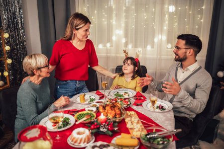 Photo for Photo captures the warmth and joy of a Christmas dinner with a beloved grandmother, mother, father, and daughter. The family is gathered around the festive table, smiling and laughing as they enjoy a traditional feast of turkey, stuffing, and all the - Royalty Free Image