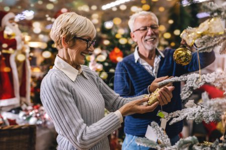 Photo for Senior couple at Christmas Market buying decor toys and balls. Concept of Christmas and New Year shopping. - Royalty Free Image