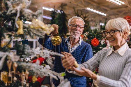 Téléchargez les photos : Couple aîné au marché de Noël acheter des jouets de décoration et des balles. Concept de Noël et du Nouvel An shopping. - en image libre de droit