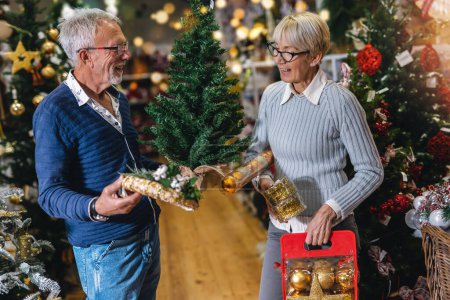 Photo for Senior couple at Christmas Market buying decor toys and balls. Concept of Christmas and New Year shopping. - Royalty Free Image