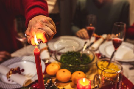 Téléchargez les photos : Allumer une bougie sur la table à manger. Famille ayant dîner de Noël. - en image libre de droit