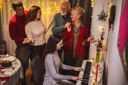 Photo for Granddaughter playing a piano for her family on Christmas Eve. - Royalty Free Image