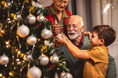 Foto de Familia decorando juntos un árbol con luces y bolas. Tiempo de Navidad. - Imagen libre de derechos