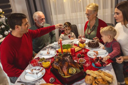 Foto de Familia feliz cenando Vhristmas con sus abuelos. Comer comida casera, beber bebidas. Casa está decorada para la víspera de Año Nuevo y Navidad - Imagen libre de derechos