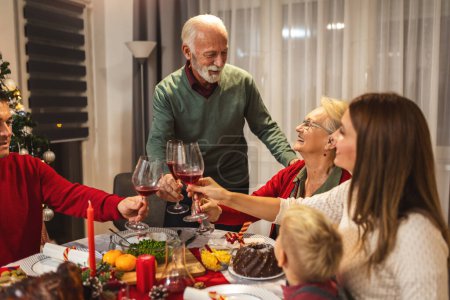Foto de El abuelo hace un brindis en la mesa. Familia celebrando la Navidad juntos comiendo comida casera. - Imagen libre de derechos