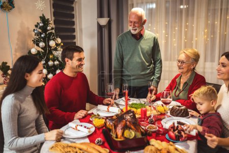 Photo for Grandfather is making a toast at the table. Family celebrating Christmas together eating homemade food. - Royalty Free Image