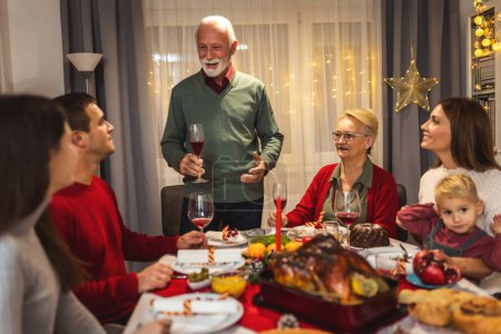 Téléchargez les photos : Grand-père porte un toast à table. Famille célébrant Noël ensemble manger de la nourriture maison. - en image libre de droit