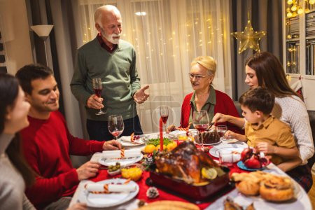 Photo for Grandfather is making a toast at the table. Family celebrating Christmas together eating homemade food. - Royalty Free Image