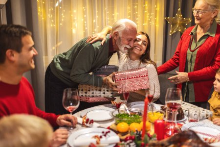 Foto de Abuelos dando regalos a sus nietos en Nochebuena. Familia cenando. - Imagen libre de derechos