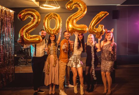 Foto de Grupo de jóvenes celebrando el Año Nuevo en el club nocturno. Están sosteniendo globos dorados. - Imagen libre de derechos