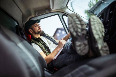Téléchargez les photos : Un conducteur de camion fatigué prend une pause de la conduite et se repose dans son camion - en image libre de droit
